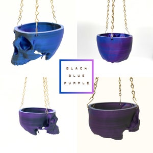 May include: Three hanging skull planters in different color variations: black, blue, and purple. The planters are made of a 3D printed material and have a smooth, glossy finish.