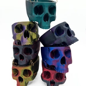 May include: A stack of six hanging skull planters in various iridescent colors, including teal, purple, black, blue, green, and red.