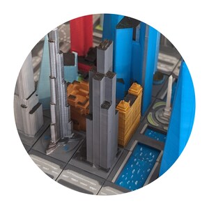 May include: A model of a city skyline with buildings in various colours, including grey, blue, and orange. The buildings are arranged in a grid pattern on a grey surface.