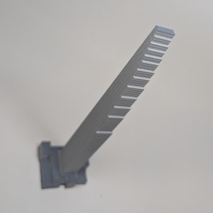 May include: A grey, elongated, rectangular component featuring a series of evenly spaced, horizontal notches along one side. The object has a textured, grid-like pattern on its surface and is attached to a wider, square-shaped base at the bottom.