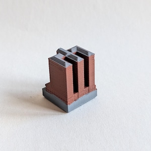 May include: A small, three-dimensional architectural model of a building with a rectangular grey base. The structure features reddish-brown walls with vertical recessed sections and a flat, dark grey roof, showcasing a layered, printed texture.