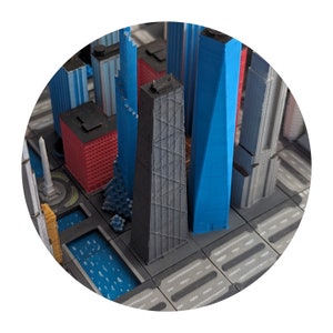 May include: A close-up of a 3D printed model of a city skyline. The model features several tall buildings, including a gray skyscraper with a grid pattern, a blue skyscraper, and a red building. The buildings are arranged on a gray base with black lines representing streets.