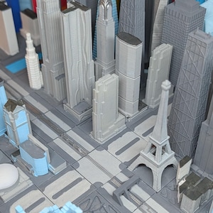 May include: A detailed miniature cityscape model featuring various skyscrapers and iconic structures, including a replica of the Eiffel Tower. The buildings are primarily shades of grey and white, set on a grey base with road details.