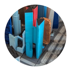 Peut inclure: Gros plan d'une maquette de ville miniature avec des bâtiments en plastique bleu, rouge et marron. Les bâtiments sont disposés sur une base grise et blanche.
