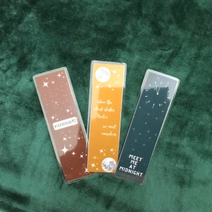 May include: Three decorative bookmarks with a celestial theme. The bookmarks are made of cardstock and feature a moon, stars, and the text "Meet Me At Midnight".