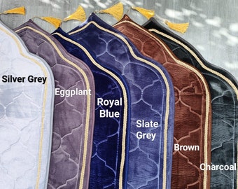 May include: A set of seven prayer rugs in various colors, including silver grey, eggplant, royal blue, slate grey, brown, and charcoal. Each rug has a gold trim and a tassel.