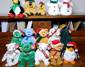 May include: A collection of 14 beanie baby plush toys, including a snowman, penguin, and various animals. The toys are arranged on a wooden surface with a brown background.