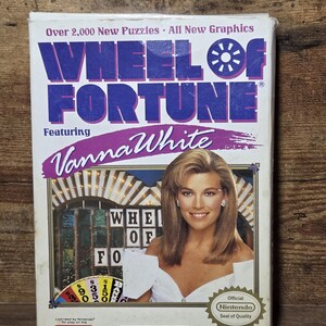 Puede incluir: Caja de videojuego vintage Wheel of Fortune con Vanna White. La caja tiene un fondo blanco con texto morado y azul. La caja también incluye el sello de calidad de Nintendo y el logotipo de GameTek.