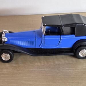 May include: A blue vintage toy car with a black convertible top. The car has silver-colored accents on the headlights, wheels, and front bumper. The toy car is approximately 8 inches long.
