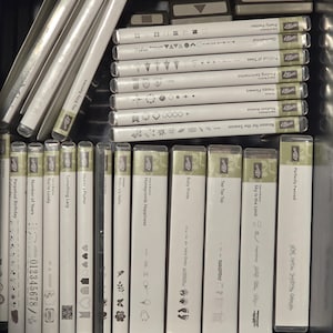 May include: A selection of white and clear stamp sets and punches, arranged in a black storage container. The stamps display diverse designs and text, such as "Happy Flowers," "Baby Prints," and "Itty Bitty Banners."