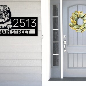 Puede incluir: Placa de n&uacute;mero de casa de metal negro con un perro blanco asom&aacute;ndose por la parte superior y el texto "2513 MAIN STREET" debajo.