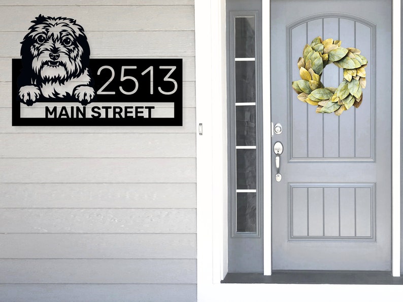 Puede incluir: Placa de n&uacute;mero de casa de metal negro con un perro blanco asom&aacute;ndose por la parte superior y el texto "2513 MAIN STREET" debajo.
