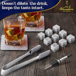 May include: Set of gray granite whiskey stones with a pair of stainless steel tongs and a bottle pourer. The stones are on a wooden surface with two glasses of whiskey and coasters. The text "A Touch of Wonders - Life's Little Joys" is on a blue and white label.