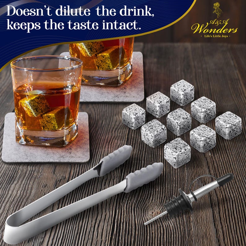 May include: Set of gray granite whiskey stones with a pair of stainless steel tongs and a bottle pourer. The stones are on a wooden surface with two glasses of whiskey and coasters. The text "A Touch of Wonders - Life's Little Joys" is on a blue and white label.
