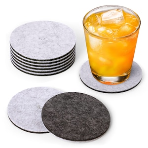 May include: A set of 10 round felt coasters in gray and black. The coasters are stacked in a pile, with a glass of orange juice on top of one of the coasters.
