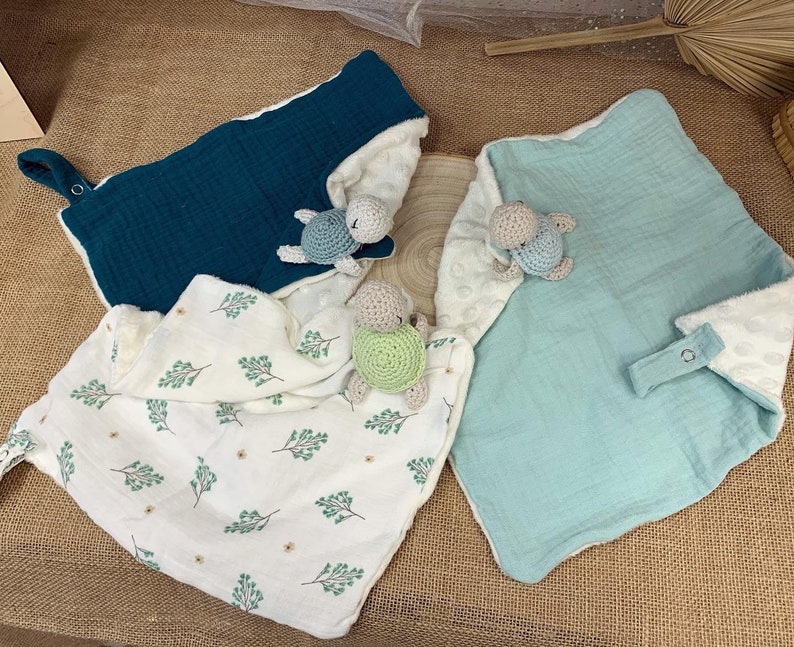 May include: Three baby blankets with crocheted turtle toys. The blankets are made of soft, textured fabric and come in teal, light blue, and white with a green leaf pattern.