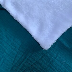 May include: A soft, plush blanket with a teal green side and a white side. The blanket is folded in half, showing both sides.