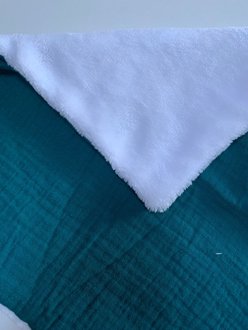 May include: A soft, plush blanket with a teal green side and a white side. The blanket is folded in half, showing both sides.