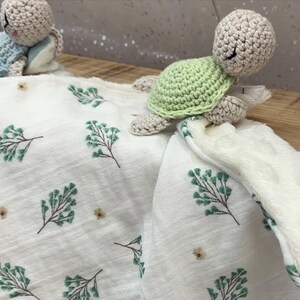 May include: A white baby blanket with a green leafy pattern and two crocheted turtle toys. One turtle is green and the other is beige.