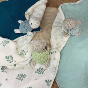 May include: Three crocheted turtle toys on a white, green, and blue fabric background. The turtles are different colors and have different colored shells.