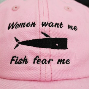 May include: Pink baseball cap with black embroidered text that reads "Women want me Fish fear me" and a black silhouette of a fish.