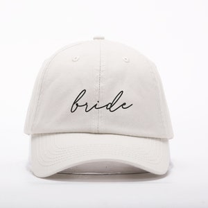 May include: A white baseball cap with the word "bride" embroidered in black cursive script.