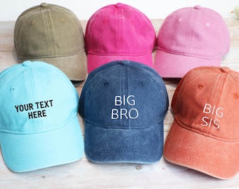 Puede incluir: Seis gorras de béisbol en varios colores, incluyendo verde oliva, rosa intenso, rosa claro, azul claro, azul marino y naranja. La gorra azul claro tiene el texto "YOUR TEXT HERE", la gorra azul marino dice "BIG BRO" y la gorra naranja dice "BIG SIS".