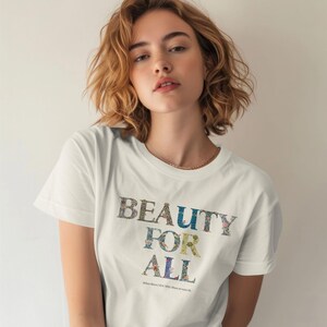 A woman with short, light brown hair wears a cream t-shirt with "BEAUTY FOR ALL" printed in floral and nature-themed patterns.