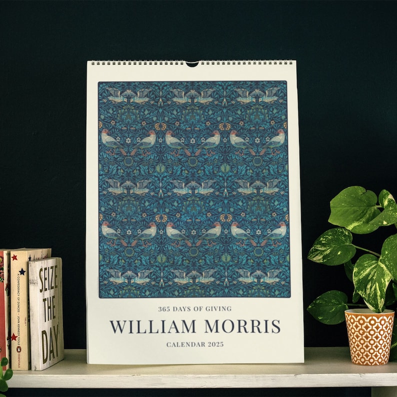 Decorative William Morris 2025 wall calendar against a black background, with a bird and foliage design in blues and greens.