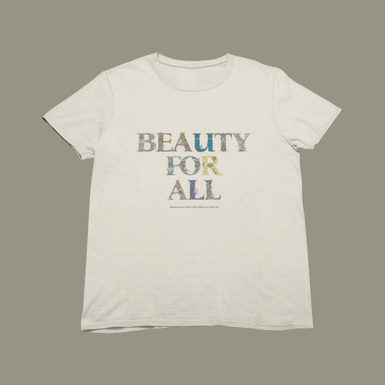 A cream-colored short-sleeved t-shirt with the words "BEAUTY FOR ALL" printed on the front in floral and nature-themed patterns, with a small quote below.