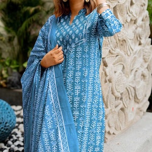 May include: A blue and white floral print tunic and scarf set. The tunic has a V-neck and long sleeves. The scarf is draped over the arm. The fabric has a repeating floral pattern. The outfit is a light blue colour.