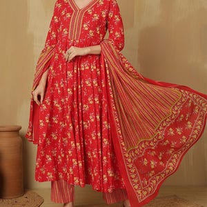 May include: A red floral print ensemble featuring a long-sleeved top with a V-neck and matching pants. The outfit includes a flowing scarf with a striped and floral pattern. The fabric is adorned with yellow floral designs.
