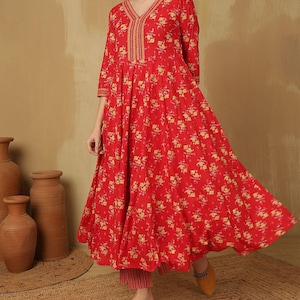 May include: A red floral print dress with a V-neckline and three-quarter sleeves. The dress features a flowing silhouette and is paired with matching pants. The outfit is adorned with yellow floral patterns and gold embroidery.