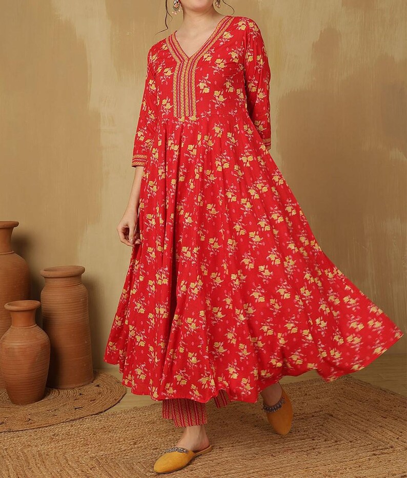 May include: A red floral print dress with a V-neckline and three-quarter sleeves. The dress features a flowing silhouette and is paired with matching pants. The outfit is adorned with yellow floral patterns and gold embroidery.