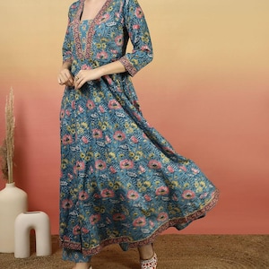 May include: A teal floral print dress with a V-neckline and three-quarter sleeves. The dress features a pink and gold floral pattern and matching pants. The outfit is paired with embroidered flats. The dress is suitable for casual or formal occasions.