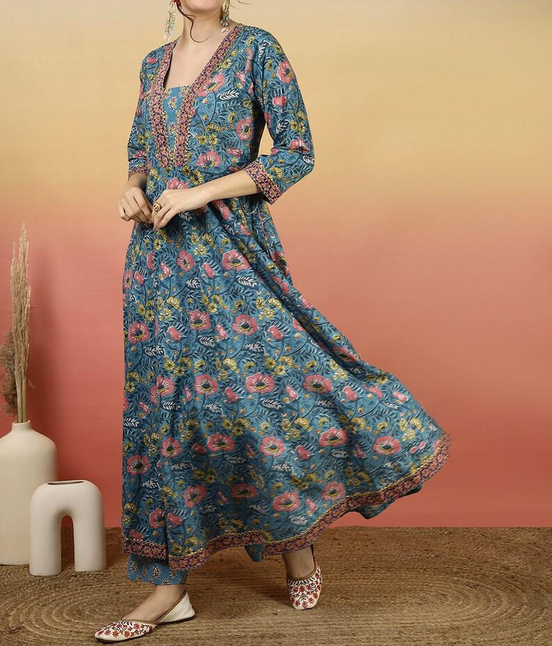 May include: A teal floral print dress with a V-neckline and three-quarter sleeves. The dress features a pink and gold floral pattern and matching pants. The outfit is paired with embroidered flats. The dress is suitable for casual or formal occasions.