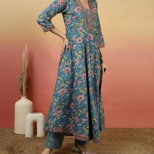 May include: A teal floral print kurta set. The long-sleeved top has a V-neck with pink embroidery and a matching floral pattern. The set includes matching pants and shoes with a floral design.