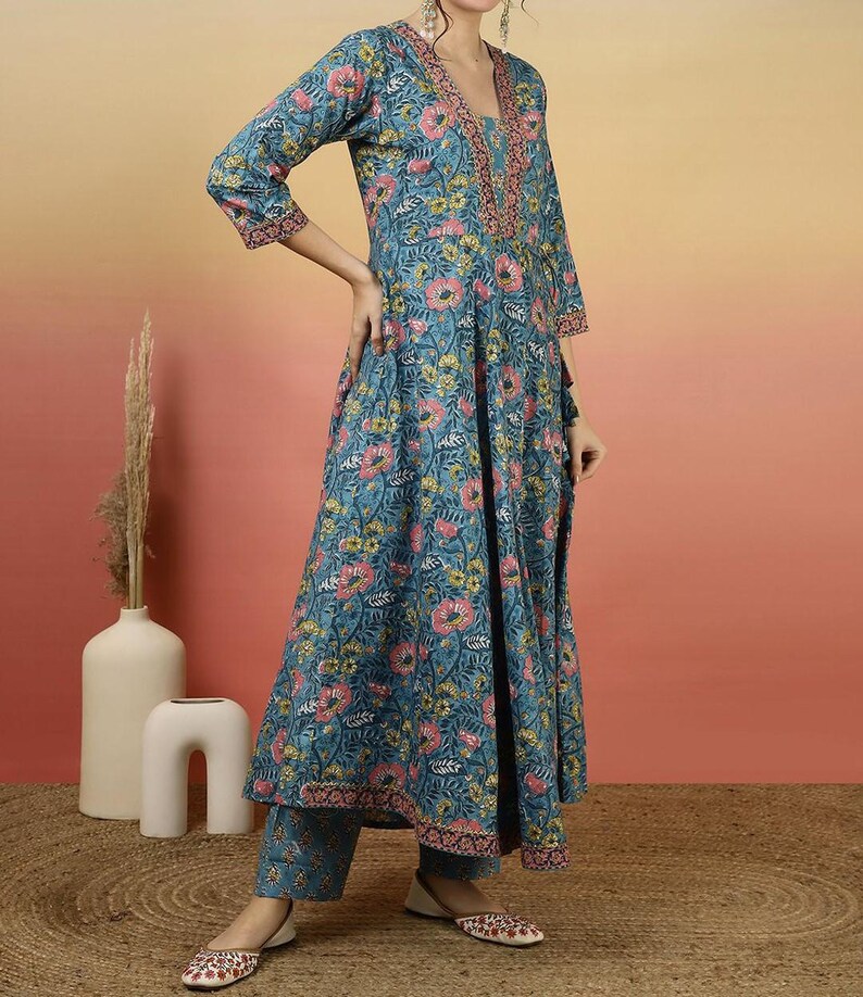 May include: A teal floral print kurta set. The long-sleeved top has a V-neck with pink embroidery and a matching floral pattern. The set includes matching pants and shoes with a floral design.