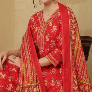 May include: A red floral print salwar kameez set. The outfit features a V-neck top with three-quarter sleeves and a matching scarf. The fabric is adorned with yellow floral patterns and intricate border designs.