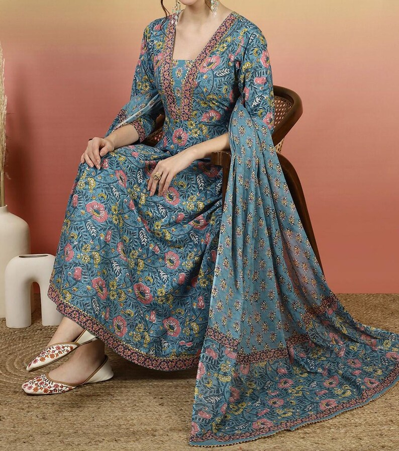 May include: A teal floral print dress with a matching shawl. The dress features a V-neckline and three-quarter sleeves. The floral pattern includes pink and yellow flowers with green leaves. The shawl is draped over the chair and has a similar floral design.
