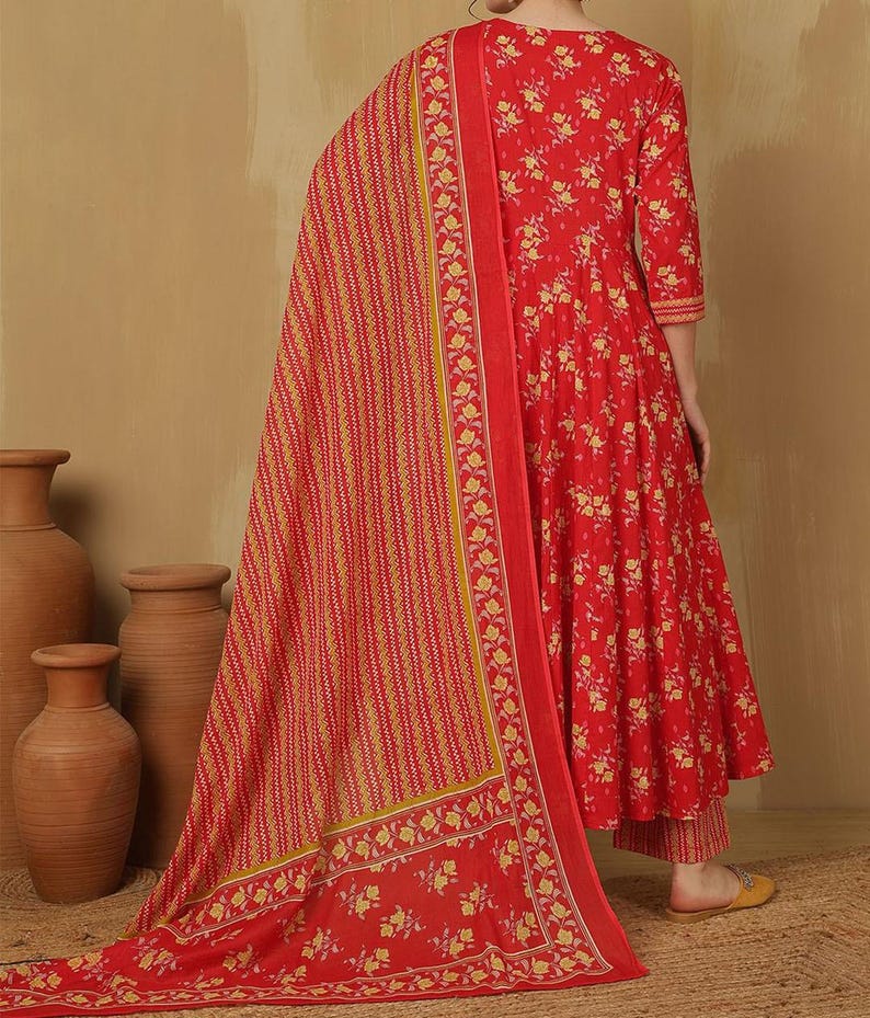 May include: A red floral print Anarkali suit with a matching dupatta. The suit features a three-quarter sleeve top and matching pants. The dupatta has a striped pattern with floral borders. The outfit is made of a lightweight fabric.