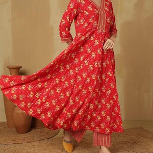 May include: A red floral print outfit featuring a long-sleeved top with a V-neck and matching pants. The top has gold embroidery around the neckline and cuffs. The outfit is paired with yellow shoes.