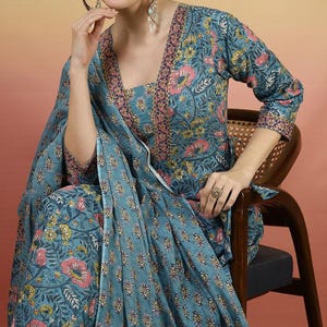 May include: A teal floral print outfit featuring a long-sleeved top and matching pants. The outfit has a square neckline and is adorned with pink and yellow flowers. The outfit is worn with a matching scarf and a ring.