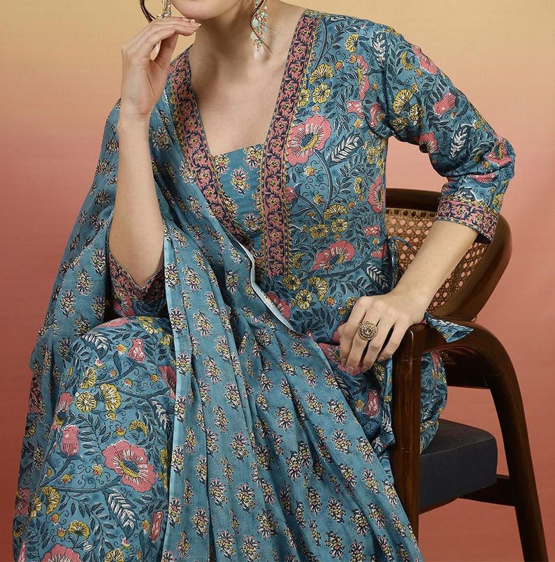May include: A teal floral print outfit featuring a long-sleeved top and matching pants. The outfit has a square neckline and is adorned with pink and yellow flowers. The outfit is worn with a matching scarf and a ring.