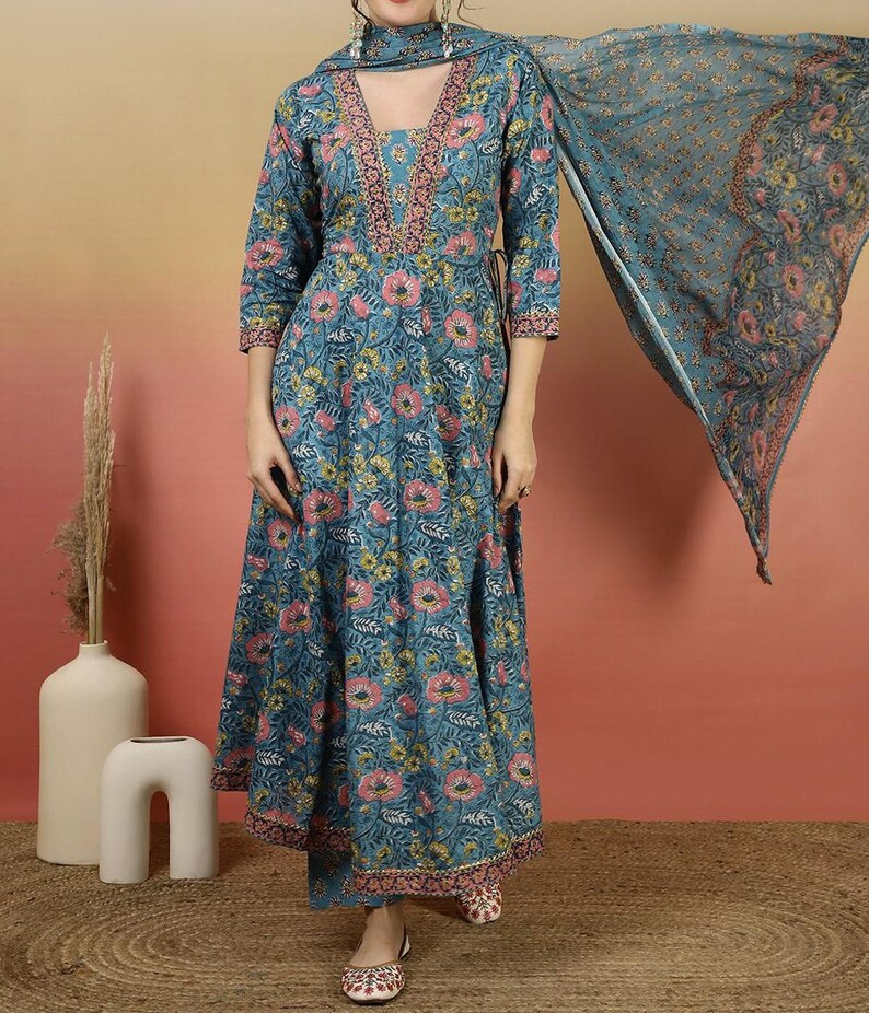 May include: A teal floral print dress with a matching scarf. The dress features a V-neckline and three-quarter sleeves. The floral pattern includes pink and yellow flowers. The outfit is paired with matching pants and shoes.