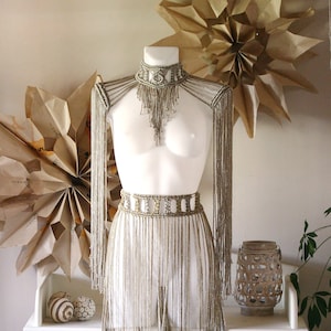 Op de afbeelding: Een zilveren kralen-fringe top en rok set met een delicate kralen choker. De set wordt getoond op een wit mannequin tegen een witte achtergrond.