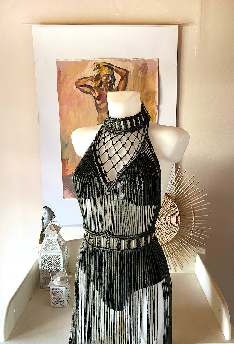 May include: A long, olive green crochet dress with a halter neckline and fringe detailing. The dress has a geometric pattern and a fitted bodice.