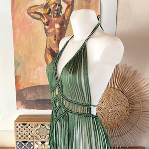 Op de afbeelding: Een groene gecrochete haltertop met franjes. De top is op een wit mannequin en heeft een diepe V-hals.