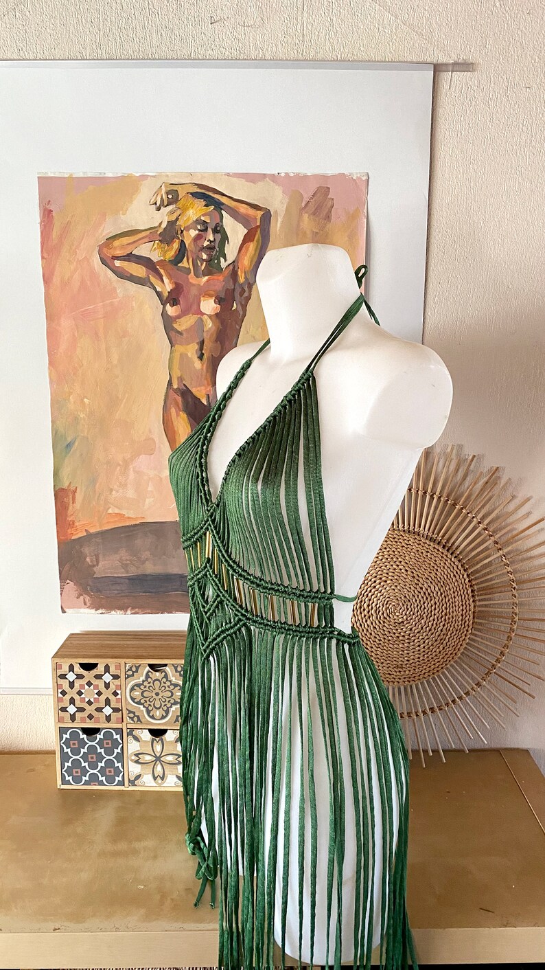 Op de afbeelding: Een groene gecrochete haltertop met franjes. De top is op een wit mannequin en heeft een diepe V-hals.