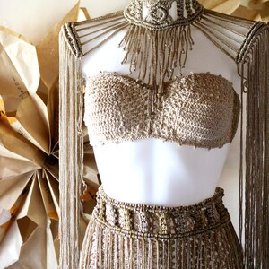 Op de afbeelding: Een gouden haltertop en rokset met franjes. De top is een bandeau-stijl en de rok is een hoge taille, aansluitende stijl.